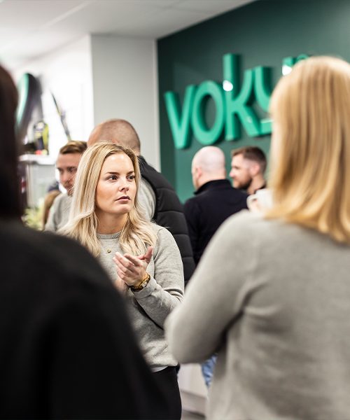 Kvinna med händerna ihop och neutral min, omgiven av Voky-anställda